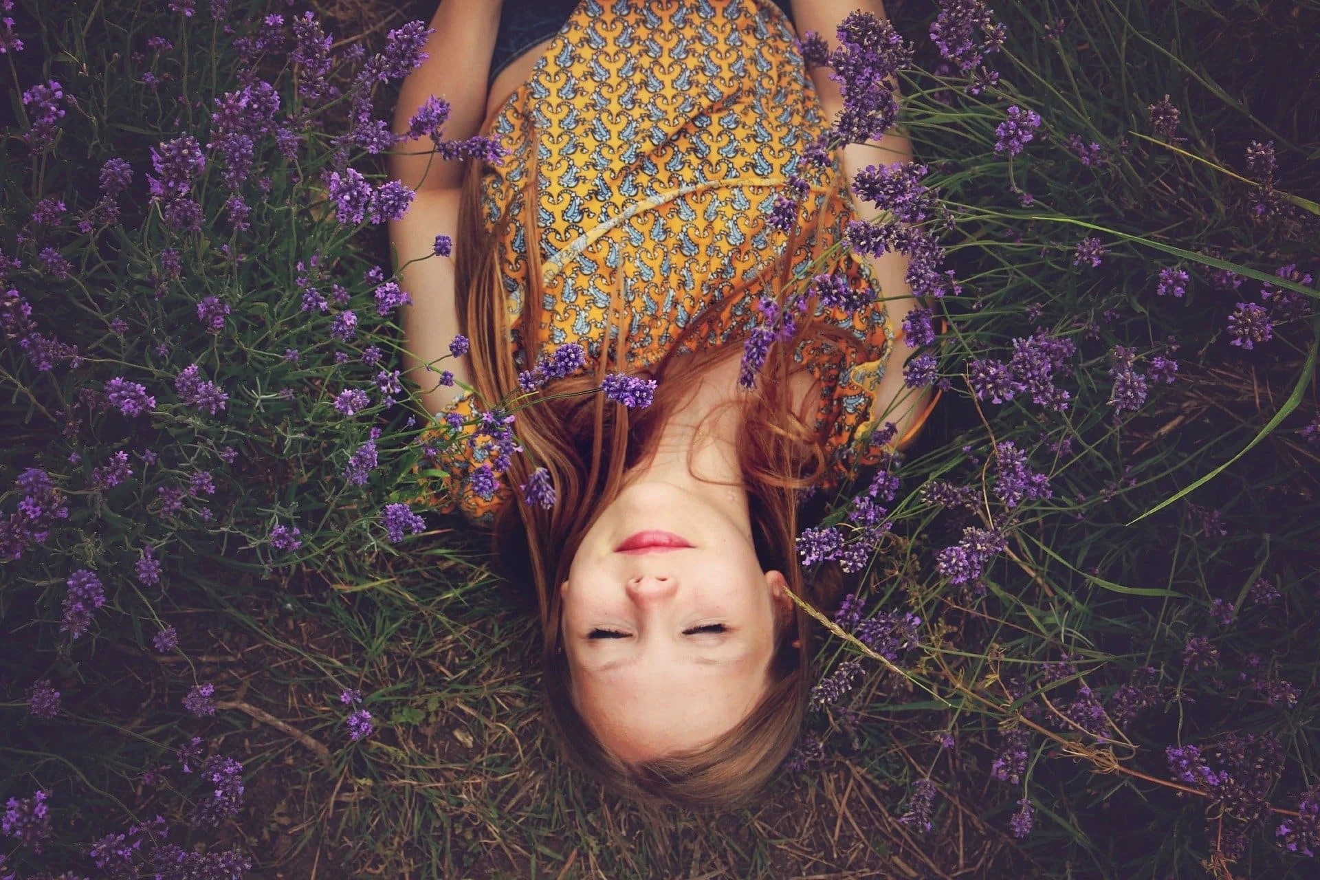 Ein Mädchen liegt entspannt in einem Feld von blühendem Lavendel, die Augen geschlossen und in tiefer Achtsamkeit versunken. Diese ruhige Szene spiegelt die Verbindung mit der Natur wider und betont die Bedeutung der Achtsamkeit, um im Moment zu leben und die Schönheit der einfachen Dinge im Leben zu schätzen.