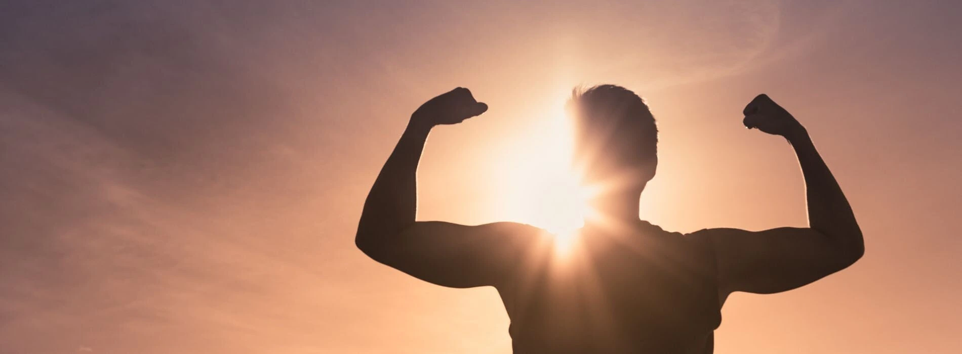 Die Silhouette eines muskulösen Mannes steht vor einem strahlenden Sonnenuntergang, die Arme in einer Pose der Stärke und des Triumphs erhoben. Diese kraftvolle Szene symbolisiert Resilienz und innere Stärke, Schlüsselelemente in der Psychotherapie, die Menschen dabei unterstützt, Herausforderungen zu überwinden und persönliches Wachstum zu fördern.