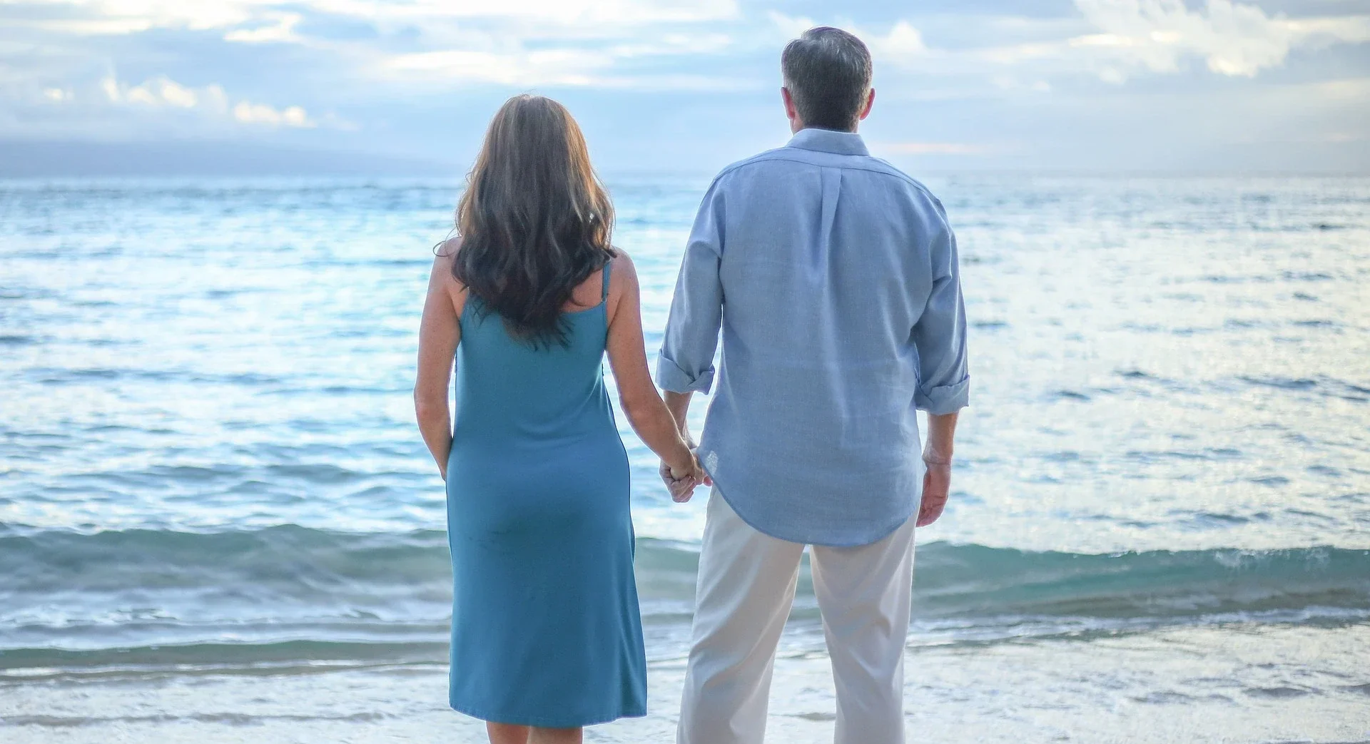 Ein Paar steht Hand in Hand am Strand, blickt gemeinsam auf das weite Meer hinaus. Sie sind von der Ruhe des Wassers und dem sanften Rauschen der Wellen umgeben, ein Symbol für tiefe Kommunikation und starke Verbindung in ihrer Beziehung. Die harmonische Szene spiegelt das gegenseitige Verständnis und die Unterstützung wider, die sie füreinander empfinden, während sie gemeinsam in die Zukunft schauen. Dieser Moment der Stille und Einheit am Meer unterstreicht die Bedeutung von nonverbaler Kommunikation und der emotionalen Bindung, die das Fundament jeder starken Beziehung bildet.