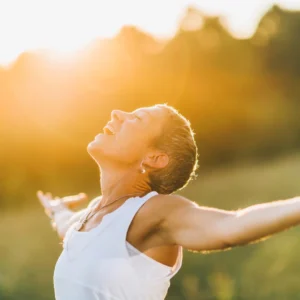 Ein Moment der Offenheit, eingefangen in einem Bild: Eine Person steht in der goldenen Stunde des Sonnenuntergangs, Arme weit geöffnet, das Gesicht zur Sonne erhoben, in einem Ausdruck purer Freude und Befreiung. Die Wärme des Lichts umhüllt die Szene, unterstreicht das Gefühl der Verbundenheit mit der Natur und der Welt. Ein Sinnbild für die Offenheit gegenüber den Geschenken des Lebens.
