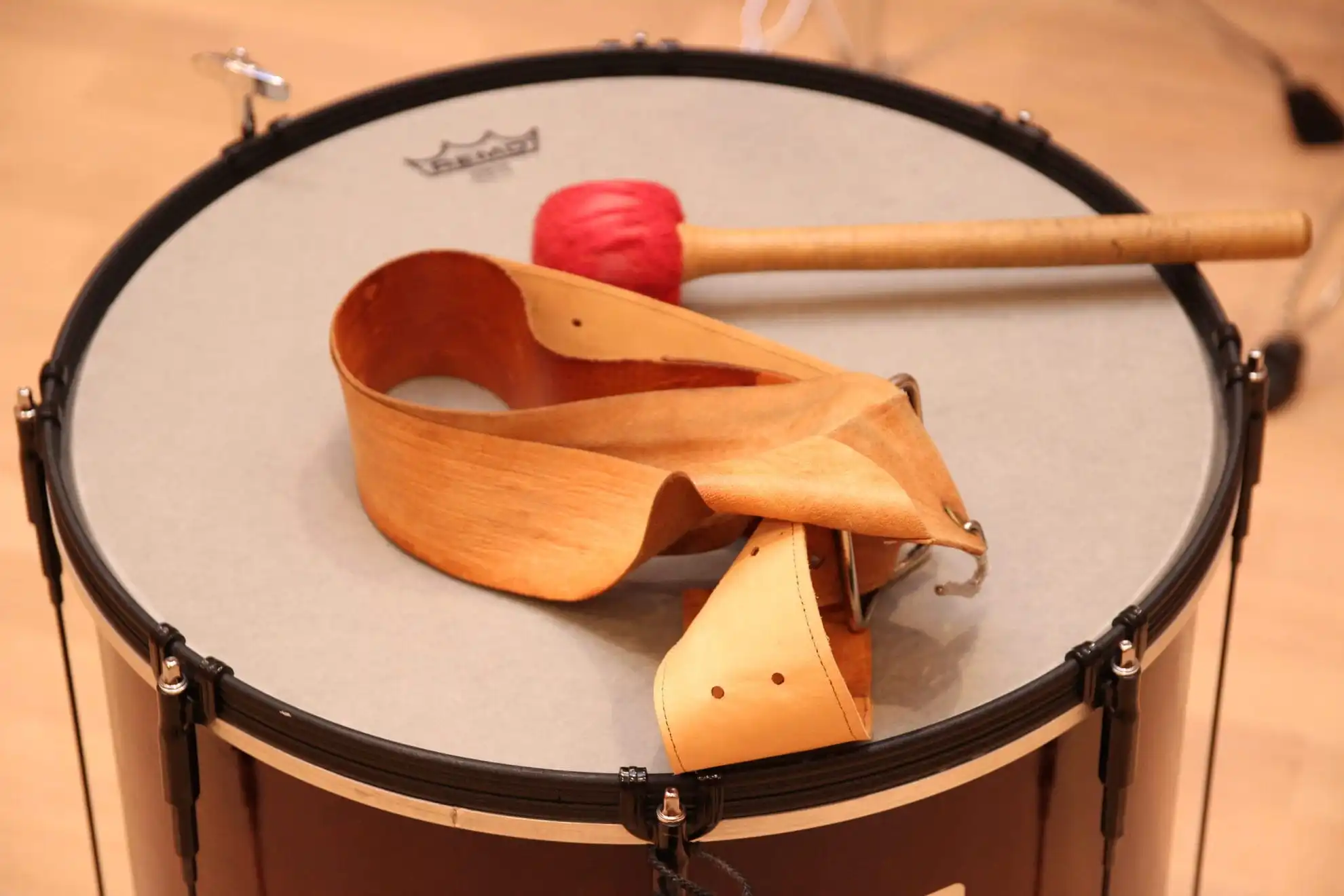 Auf dem Bild ist eine Trommel aus nächster Nähe zu sehen, die für die TaKeTiNa®-Rhythmustherapie verwendet wird. Ein roter Schlägel liegt bereit auf der Oberfläche der Trommel, daneben befindet sich ein traditioneller Holzgürtel, der typisch für diese einzigartige musiktherapeutische Methode ist. Die TaKeTiNa®-Methode nutzt Rhythmus und Musik als Mittel zur Förderung von Entspannung, Präsenz und innerer Harmonie. Diese Szene fängt die Essenz von TaKeTiNa® ein: die Verbindung von Rhythmus, Bewegung und Klang, um einen tiefen Zustand der Achtsamkeit und Selbstfindung zu erreichen.