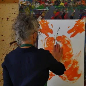 Eine Person bei einem Kreativseminar der Akademie Heiligenfeld vertieft sich in das kreative Malen, indem sie direkt mit den Händen Farbe auf eine Leinwand aufträgt. Der Hintergrund, übersät mit Farbspritzern, zeugt von der intensiven und freien künstlerischen Auseinandersetzung, die in diesen Seminaren gefördert wird.
