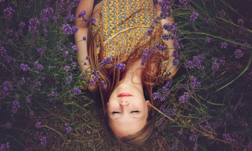 Ein Mädchen liegt entspannt in einem Feld von blühendem Lavendel, die Augen geschlossen und in tiefer Achtsamkeit versunken. Diese ruhige Szene spiegelt die Verbindung mit der Natur wider und betont die Bedeutung der Achtsamkeit, um im Moment zu leben und die Schönheit der einfachen Dinge im Leben zu schätzen.