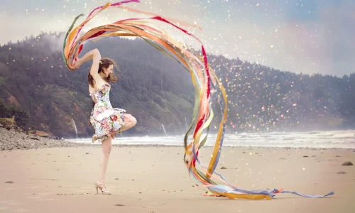Eine Frau tanzt am Strand, umgeben von lebhaften, wirbelnden Bändern, die im Wind flattern. Diese Szene verkörpert Offenheit und Selbstfindung, eingefangen in einem Moment der Freiheit und des Einklangs mit der Natur, symbolisch für die Reise zu innerem Frieden und persönlicher Entfaltung.